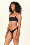Model standing to the side wearing the Muse Scoop Top and Most Wanted Bottom in Black
