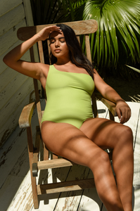 Model sunbathing in a rocking chair on porch wearing the Apex One Piece in Lime Sheen