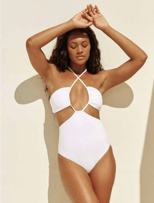 Model standing against white background with hands over her head while wearing the Layla One Piece in white