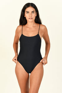 Model standing against a background while wearing the Hinge One Piece in black