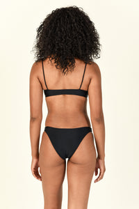 Model standing to the back wearing the Muse Scoop Top and Most Wanted Bottom in Black